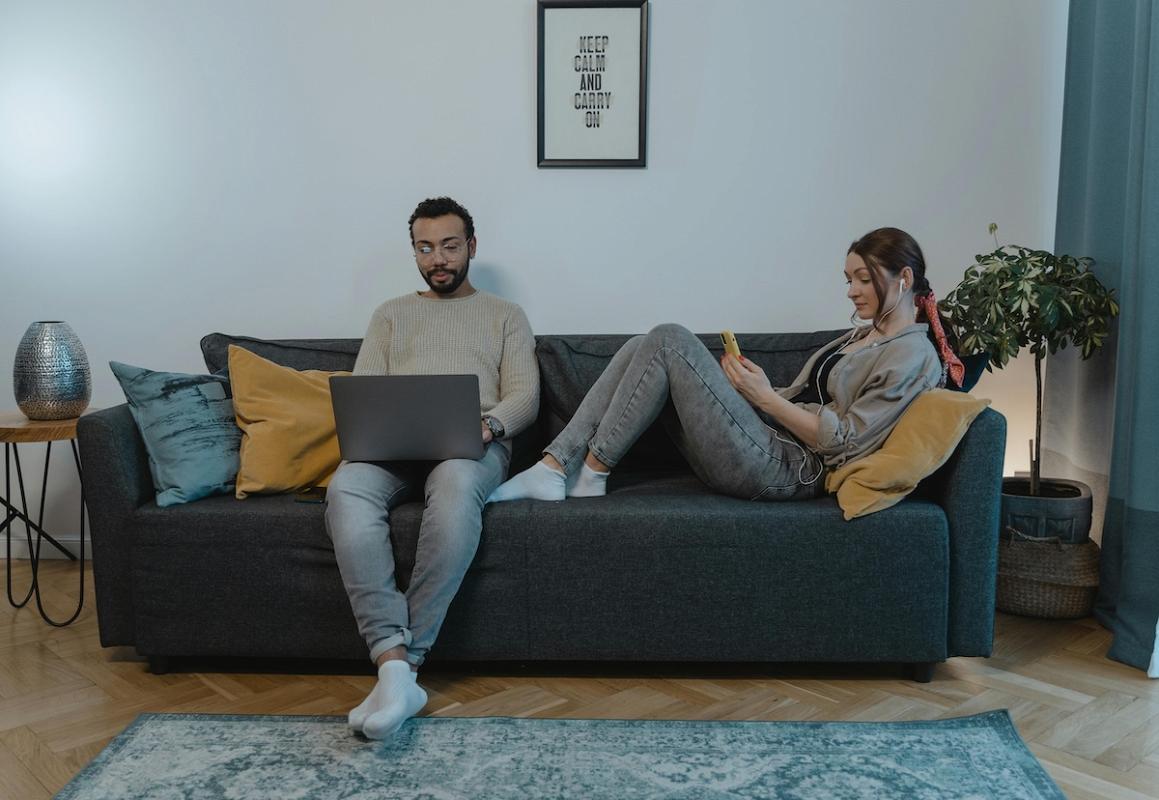 A couple relaxing on a sofa using laptop and smartphone with wireless home internet.