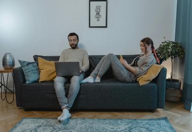 A couple relaxing on a sofa using laptop and smartphone with wireless home internet.